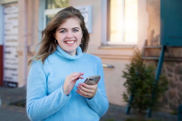 Portrait extérieur d'une fille joyeuse posant avec un téléphone dans la rue