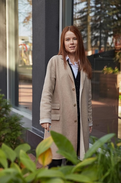 Portrait à l'extérieur d'une jeune fille à tête rouge caucasienne en manteau aux cheveux longs