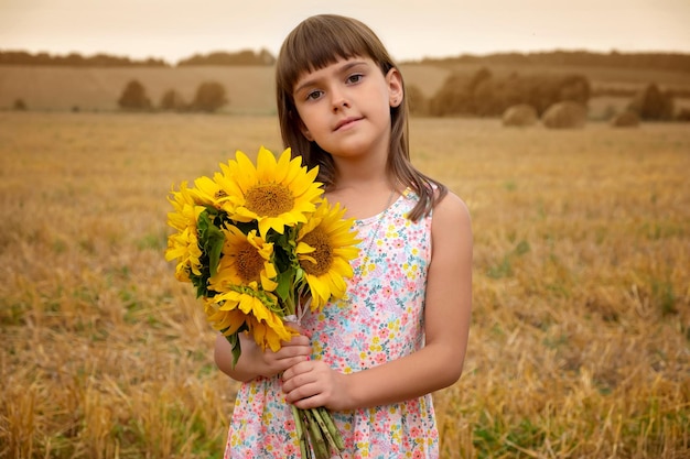 Portrait extérieur d'une petite fille avec un bouquet de tournesol dans un champ se présentant à la caméra