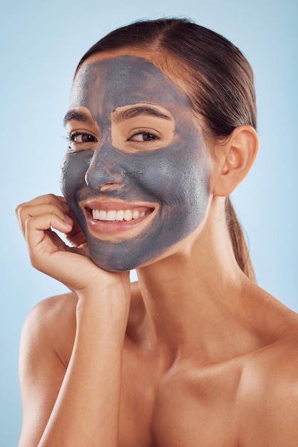 Portrait facial de femme et masque au charbon de bois pour les soins de beauté et les produits de nettoyage cosmétiques naturels sur fond bleu studio Personne ou modèle heureux dans les soins de la peau au collagène et à la boue en dermatologie