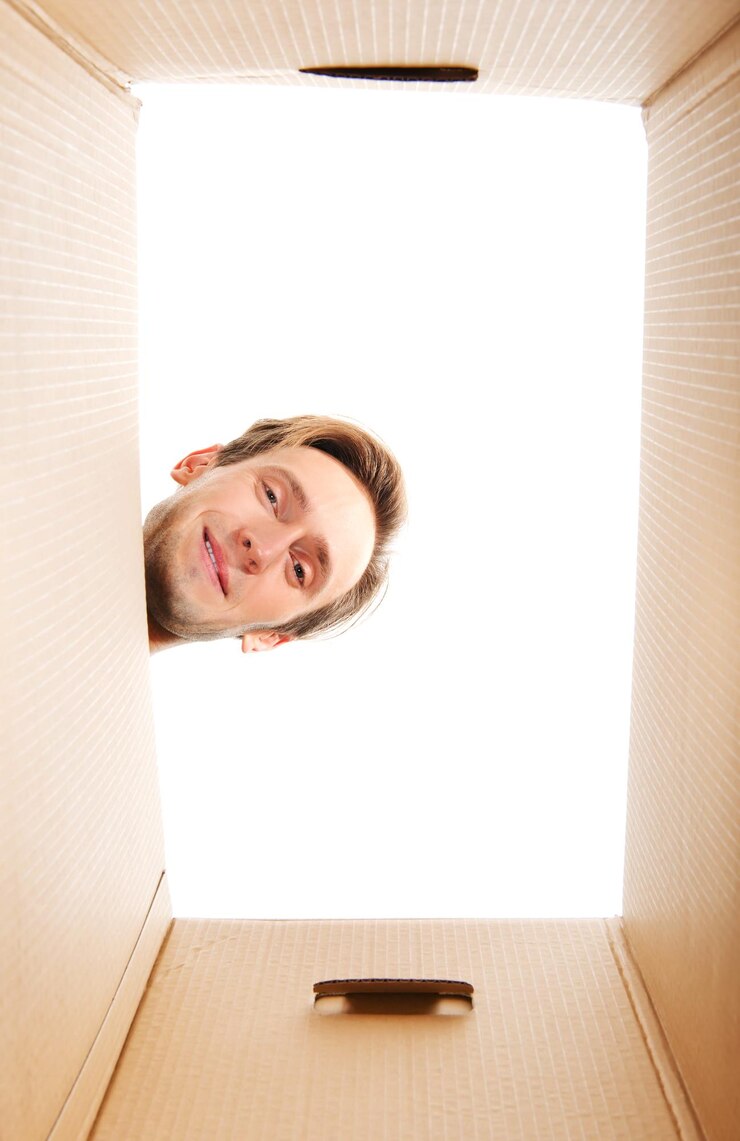 Photo portrait à faible angle d'un jeune homme regardant dans une boîte en carton contre un ciel clair