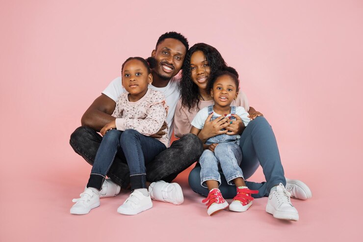 Photo portrait d'une famille afro-américaine souriante de quatre personnes assise sur le sol sur fond de studio rose