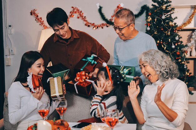 Portrait d'une famille asiatique échangeant des cadeaux pendant Noël à la maison Des gens heureux et attrayants tenant une boîte à cadeaux célèbrent la fête de Thanksgiving La tradition de la veille de Noël dans le salon de la maison ensemble