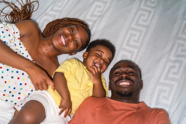Portrait d'une famille d'ethnie noire africaine avec leur petit fils dans la chambre sur le lit en souriant