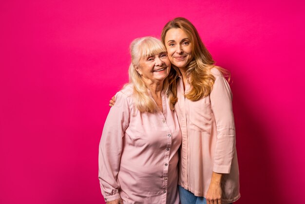 Portrait de famille, femme d'âge moyen et mère senior embrassant sur mur rose