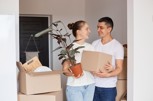 Portrait d'une famille heureuse debout avec des boîtes et des plantes dans un pot de fleurs, se regardant avec douceur et amour, étant heureux d'acheter une nouvelle maison, déménager, propriété, immobilier.