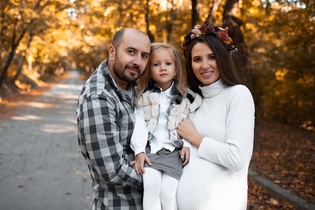 Portrait de famille heureuse sur fond de parc doré au jour d'automne Père fille et mère enceinte