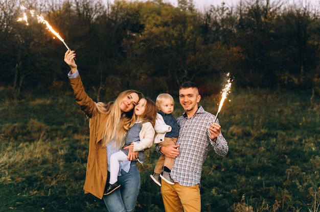 Portrait d'une famille heureuse avec des lumières du Bengale dans un champ vert au coucher du soleil