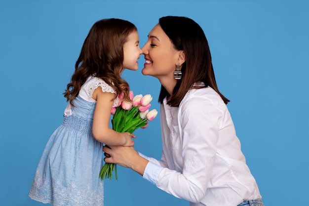 Portrait d'une famille heureuse. maman et fille se regardent et tiennent un bouquet de tulipes roses