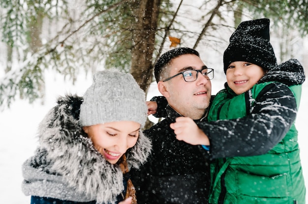 Portrait de famille heureuse, poudrerie dans le parc d'hiver. Père, mère et enfants garçon s'amusent et jouent sur une promenade hivernale enneigée dans la nature.