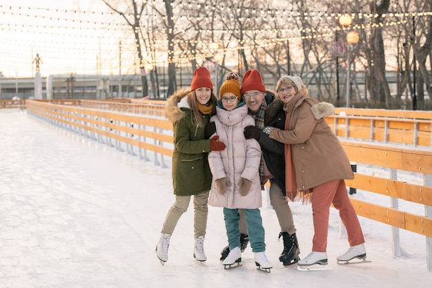 Portrait de famille heureuse s'embrassant et souriant à la caméra en patinant dans le parc