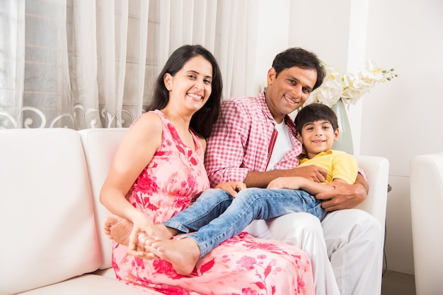 Portrait d'une famille indienne heureuse et jeune, assise sur un canapé à la maison