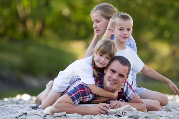 Portrait de famille de jeune mère heureuse, père et deux enfants blonds mignons, garçon et fille le jour d'été lumineux avec bokeh vert. Relations familiales heureuses, amour, soins et concept de vacances parfait