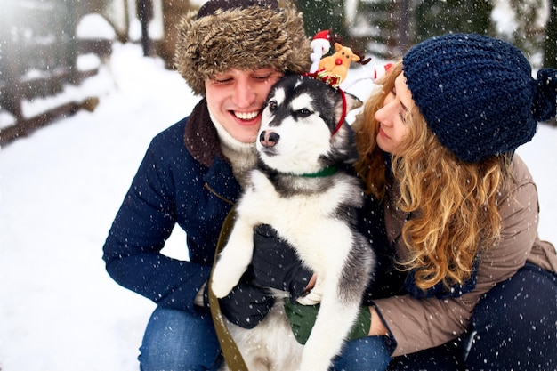 Portrait de famille d'un joli couple heureux étreignant avec leur chien malamute d'alaska léchant le visage de l'homme drôle