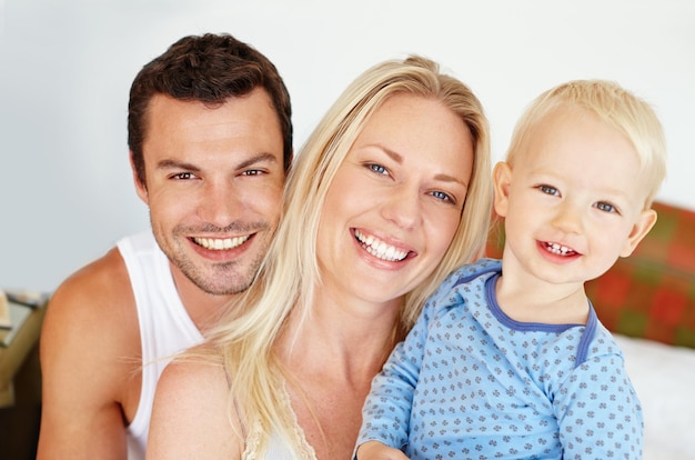 Portrait de famille parfait Deux parents souriant à la caméra avec leur jeune fils assis sur leur lit