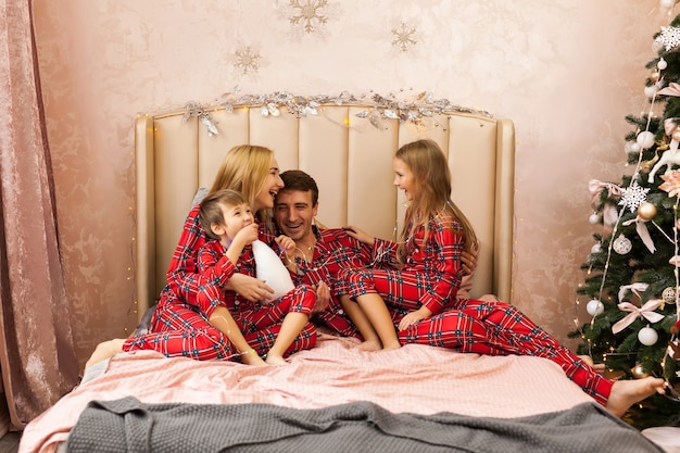 Portrait de famille en pyjama allongé sur le lit. Mère, père et deux enfants s'amusant dans la chambre. Concept de Noël et nouvel an