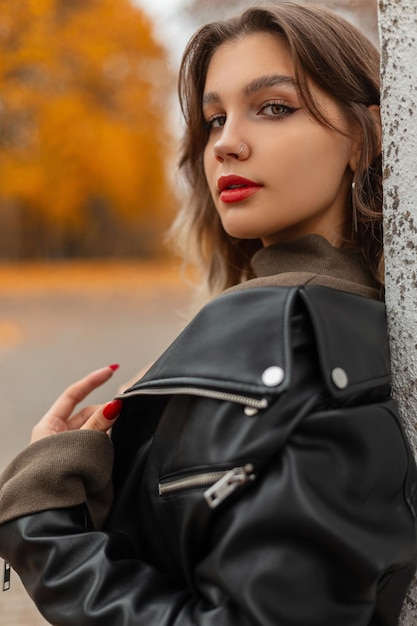 Portrait féminin d'automne d'une belle femme aux lèvres rouges dans une veste en cuir noire à la mode dans un parc d'automne doré