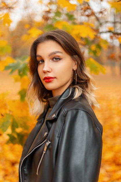 Portrait féminin d'automne d'une jolie fille élégante en veste de cuir noir fashion dans le parc d'automne jaune