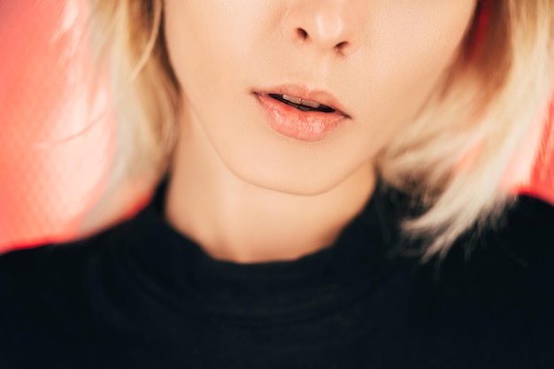 Photo portrait féminin. cosmétologie beauté. lifting du visage. contour des lèvres. procédure au laser. femme méconnaissable avec une peau parfaite isolée sur fond clair néon rouge pêche.