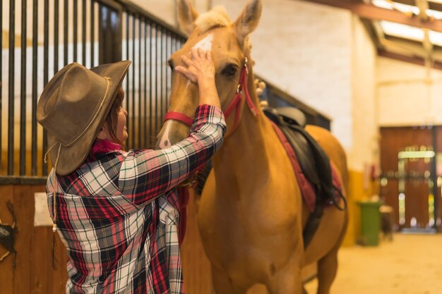 Portrait d'une femme adulte dans une écurie caressant un cheval brun, vêtue de tenues sud-américaines