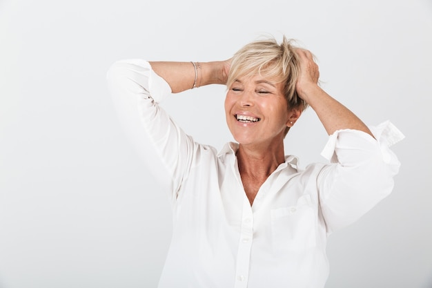 Portrait d'une femme adulte joyeuse aux cheveux blonds courts attrapant sa tête et riant à la caméra isolée sur un mur blanc en studio