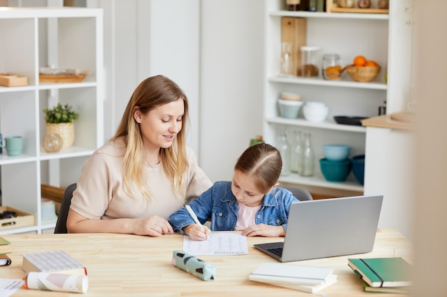 Portrait de femme adulte souriante aidant une fille à faire ses devoirs ou à étudier à la maison dans un intérieur confortable, copiez l'espace