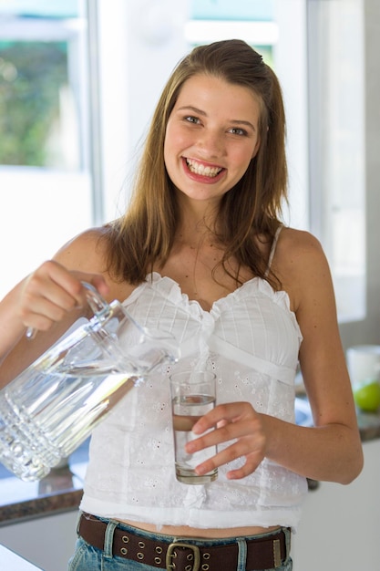 Photo portrait d'une femme adulte souriante versant de l'eau dans un verre alors qu'elle se tient dans la cuisine à la maison