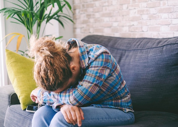 Portrait d'une femme adulte triste et bouleversée assise sur un canapé embrassant les genoux perdus dans de mauvaises pensées pessimistes souffrant seule les adultes stressés se sentent seuls désespérés ont le cœur brisé problèmes de vie féminins