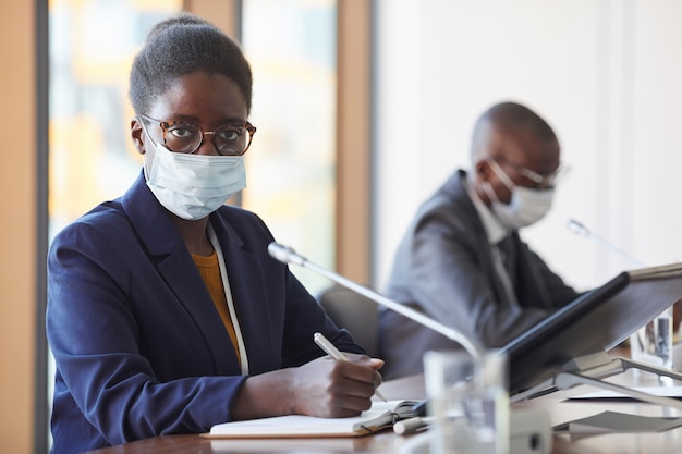 Portrait de femme d'affaires africaine en masque de protection à la recherche tout en travaillant à la conférence pendant la pandémie