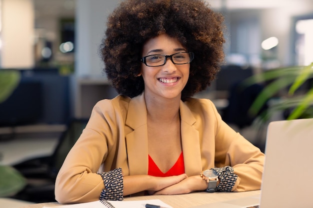 Portrait d'une femme d'affaires afro-américaine souriante assise avec un ordinateur portable sur le lieu de travail