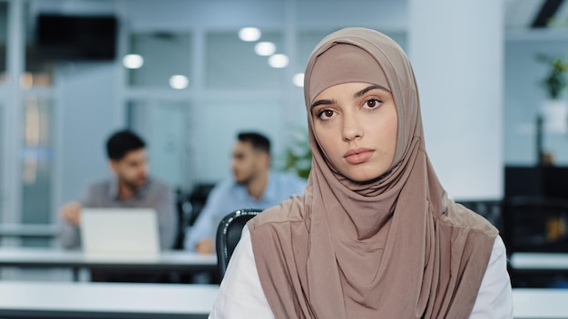 Portrait d'une femme d'affaires arabe sérieuse et agréable en hijab confiante femme courtier d'assurance directeur de banque assistante des ressources humaines dans un bureau à espace ouvert femme regardant la caméra accueillante prête à aider le client