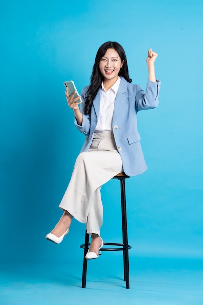 Portrait de femme d'affaires asiatique assis sur une chaise isolée sur fond bleu