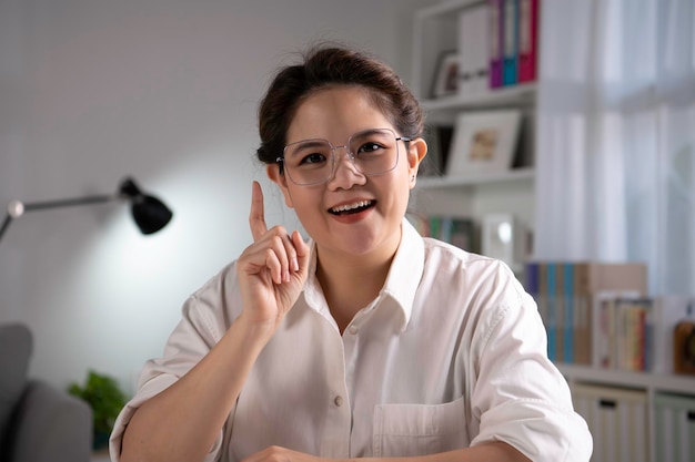 Portrait d'une femme d'affaires asiatique heureuse, amicale et confiante, assise sur un canapé à la maison, regardant et parlant à la caméra et agitant la main en disant bonjour pendant l'appel vidéo