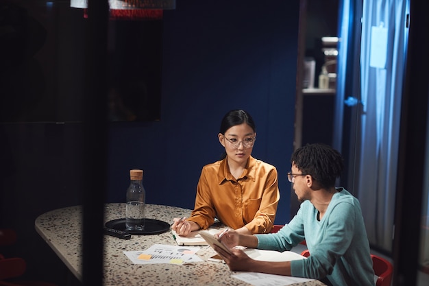 Portrait de femme d'affaires asiatique parlant à un collègue tout en travaillant tard dans un bureau sombre, espace de flic