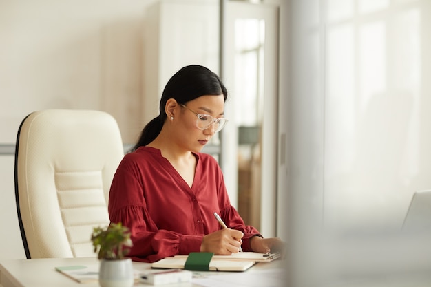 Portrait de femme d'affaires asiatique réussie portant chemisier rouge travaillant au bureau dans un bureau blanc moderne, espace copie