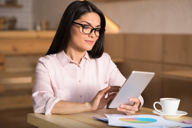 Portrait d'une femme d'affaires confiante portant des lunettes à l'aide d'une tablette numérique dans un café