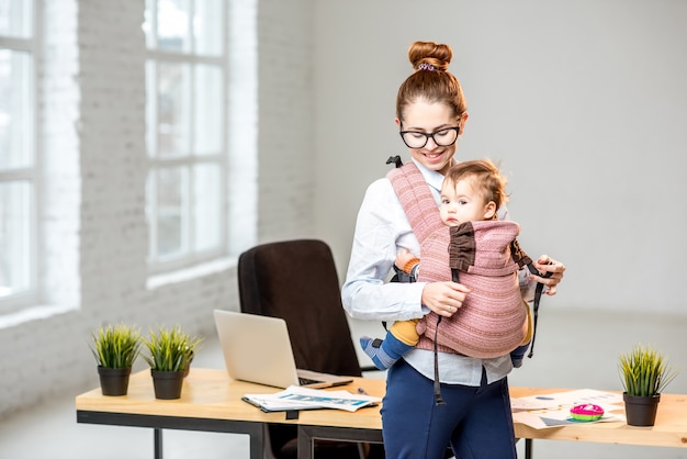 Portrait d'une femme d'affaires debout avec son bébé à l'intérieur du bureau blanc pendant la pause