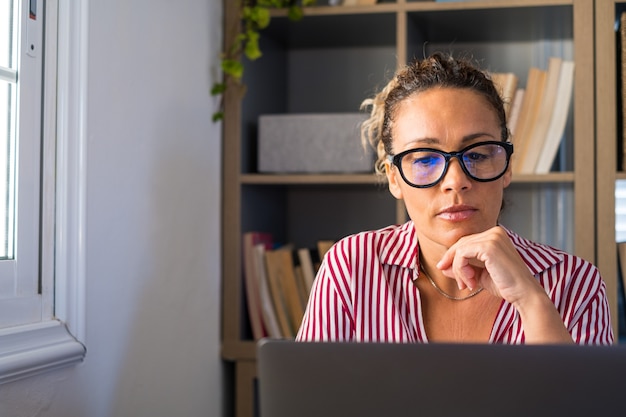 Portrait d'une femme d'affaires focalisée travaillant à domicile au bureau à l'aide d'un ordinateur portable ou d'un appareil technologique. Personne de sexe féminin portant des lunettes en regardant l'écran