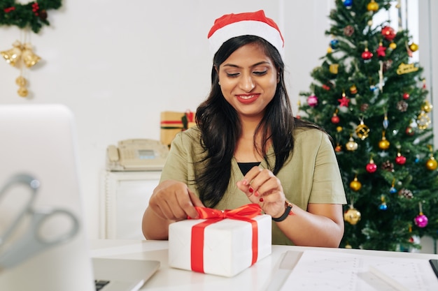 Portrait de femme d'affaires indienne souriante ouvrant le cadeau de Noël