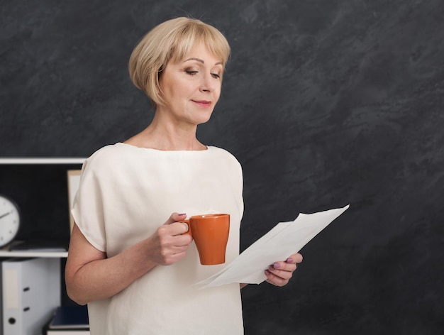 Portrait de femme d'affaires mature au travail. Avocat lisant des documents et buvant du café au bureau