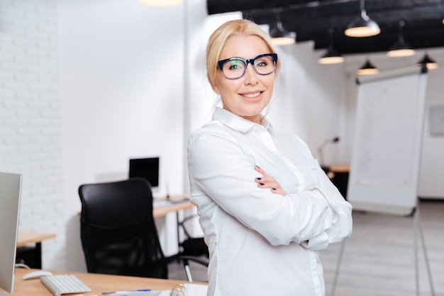 Portrait d'une femme d'affaires mature gaie debout avec les bras croisés au bureau