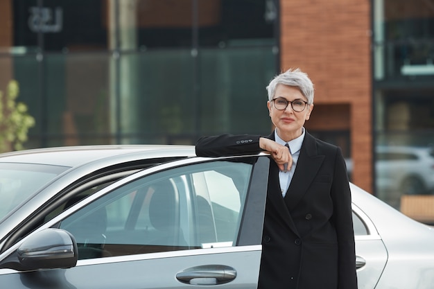 Portrait de femme d'affaires mature à lunettes debout près de la voiture