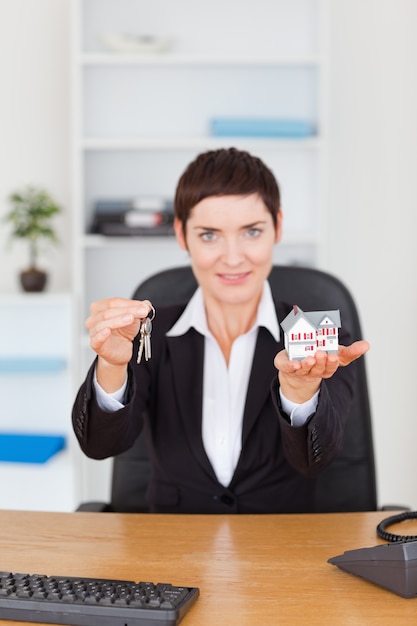 Portrait d&#39;une femme d&#39;affaires montrant une maison miniature et une clé