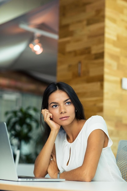 Portrait d'une femme d'affaires pensive assise à la table au bureau et regardant loin