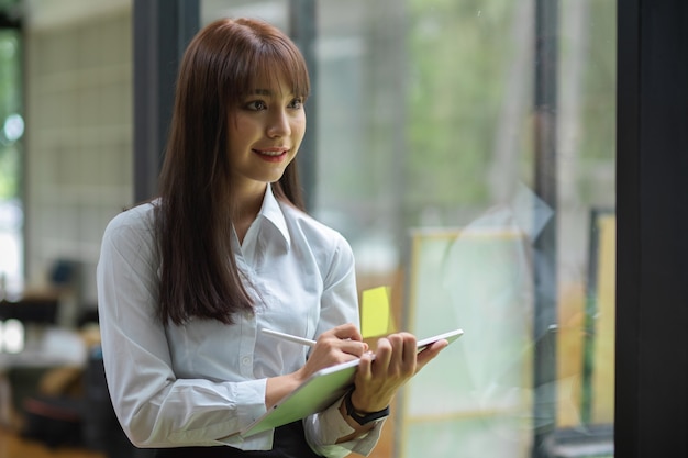 Portrait de femme d'affaires prenant note sur tablette avec stylet en position debout