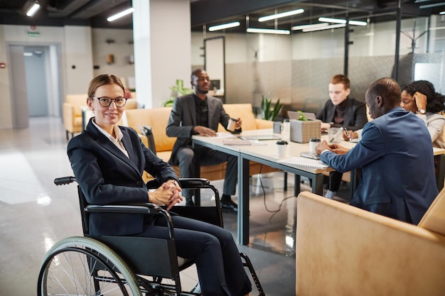 Portrait d'une femme d'affaires prospère utilisant un fauteuil roulant lors d'une réunion et regardant la caméra en souriant