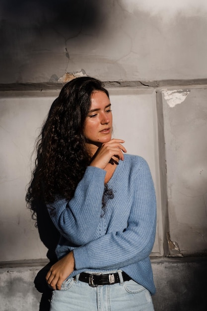 Portrait d'une femme d'affaires séduisante aux cheveux bouclés pose sur fond de mur gris