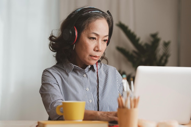 Portrait d'une femme d'affaires senior asiatique portant un casque et avec du café à l'aide d'un appel vidéo le matin à la maison Concept de compte et de finances