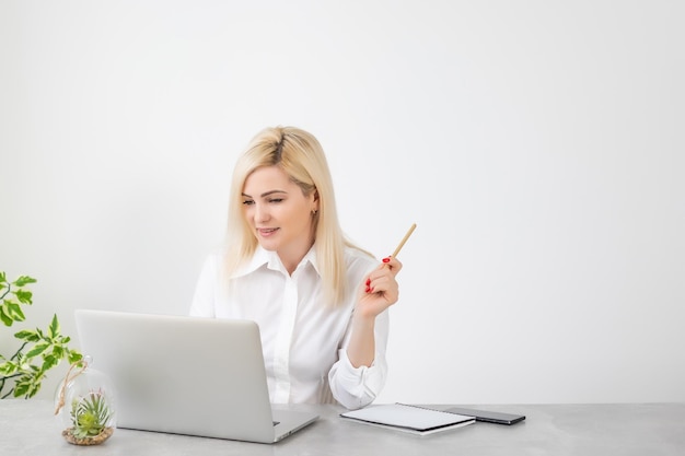 Portrait d'une femme d'affaires sérieuse utilisant un ordinateur portable au bureau contre un mur blanc