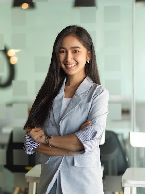 Portrait de femme d'affaires souriant et bras croisés debout dans la salle de bureau